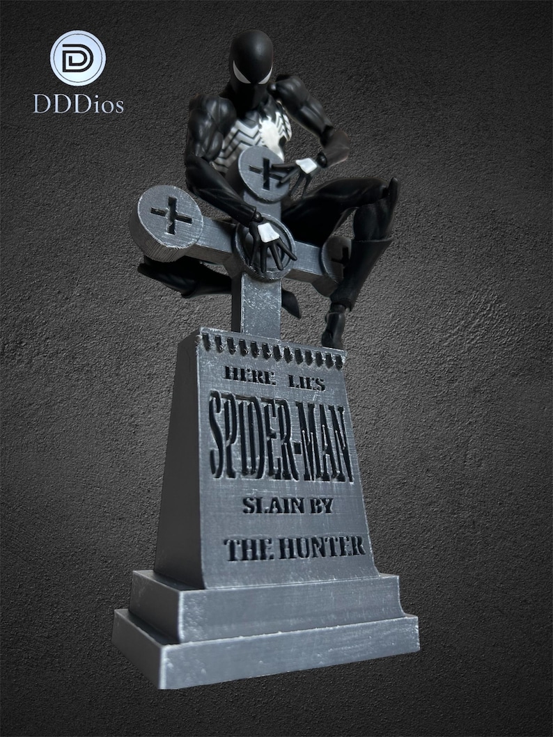 May include: A black and white Spider-Man action figure sits atop a gray tombstone. The tombstone reads "Here Lies Spider-Man, Slain by The Hunter." The figure is detailed with a white spider emblem on the chest.