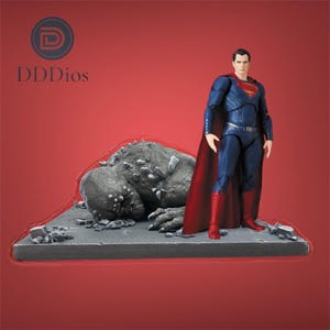 Può includere: Una action figure di Superman è in piedi sopra una figura di Doomsday sconfitto. Superman indossa un costume blu con mantello e stivali rossi. Doomsday è un mostro grigio e spinoso su una piattaforma grigia.