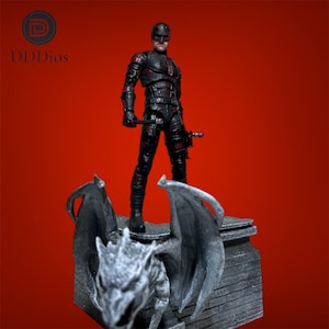 Può includere: Action figure nera di un supereroe in tuta nera con dettagli rossi, in piedi su una statua di gargoyle in pietra. La figura tiene due manganelli. Lo sfondo è di colore rosso pieno.