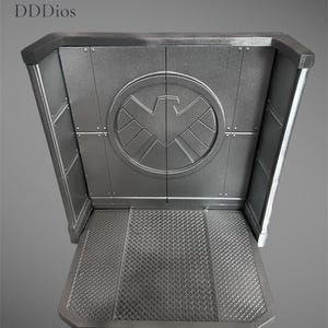 May include: A silver-colored display stand with a textured floor and a circular emblem featuring a stylized bird. The stand has a rectangular shape with angled sides and the text "DDDios" in the upper left corner.