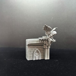 Pode incluir: Uma miniatura cinzenta de uma g&aacute;rgula de pedra impressa em 3D com asas pousada numa parede de pedra com uma pequena porta arqueada.