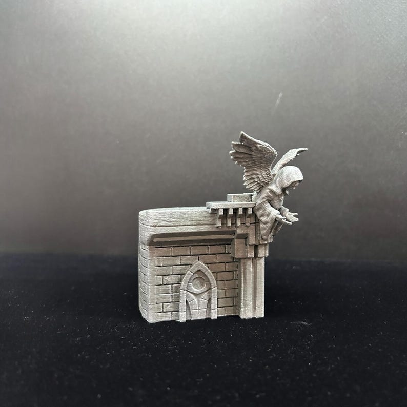 Pode incluir: Uma miniatura cinzenta de uma g&aacute;rgula de pedra impressa em 3D com asas pousada numa parede de pedra com uma pequena porta arqueada.