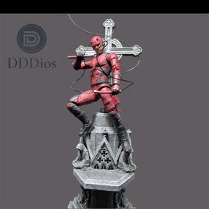 May include: A red action figure of a superhero in a dynamic pose, holding a weapon, atop a detailed stone structure. The figure is clad in a textured red suit with black boots. A cross-shaped emblem is behind the figure.