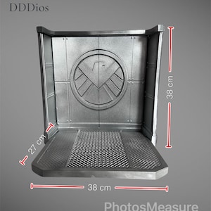May include: A silver-colored display stand with a textured base and a back panel featuring a circular emblem. The stand measures 15 inches wide, 15 inches high, and 10.6 inches deep. The stand has the text "DDDios" and "PhotosMeasure".