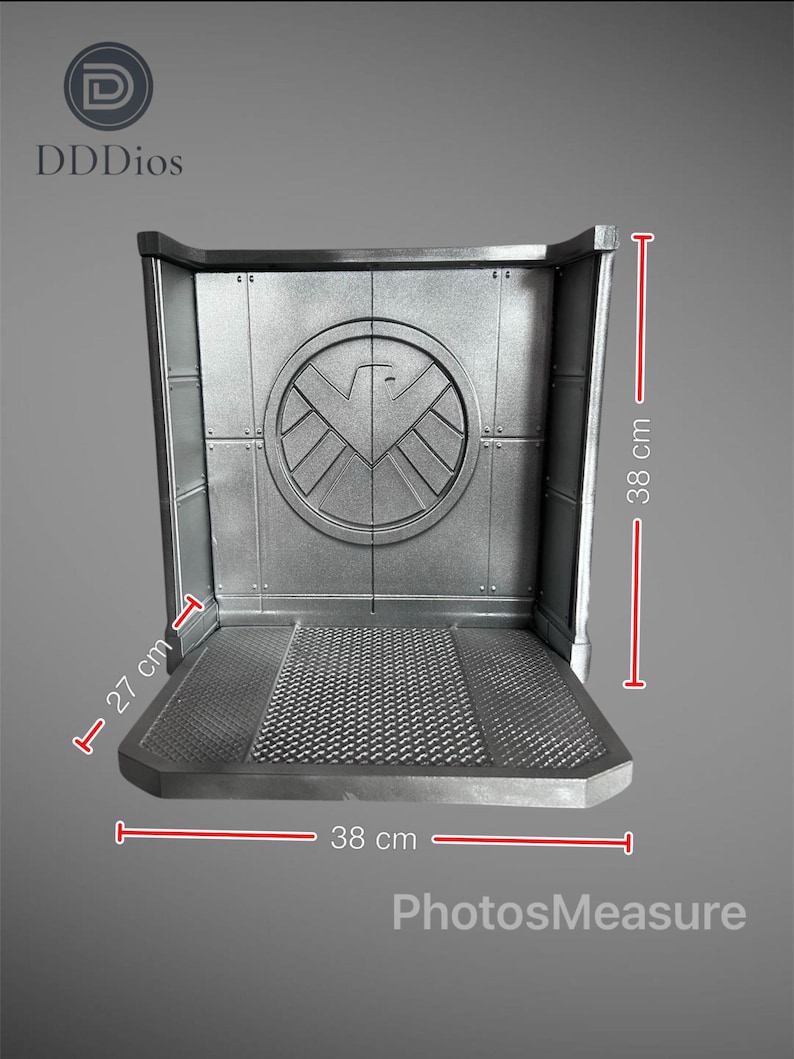 May include: A silver-colored display stand with a textured base and a back panel featuring a circular emblem. The stand measures 15 inches wide, 15 inches high, and 10.6 inches deep. The stand has the text "DDDios" and "PhotosMeasure".