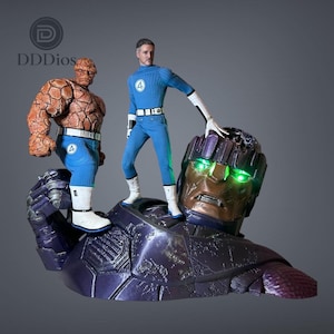 Könnte beinhalten: Ein Sammlerfiguren-Set bestehend aus einer felsigen orangefarbenen Kreatur und einer menschlichen Figur im blauen Anzug mit einer Vier als Emblem, die beide auf einem großen, metallisch violetten Roboterkopf mit leuchtend grünen Augen und dem Text DDDios stehen.