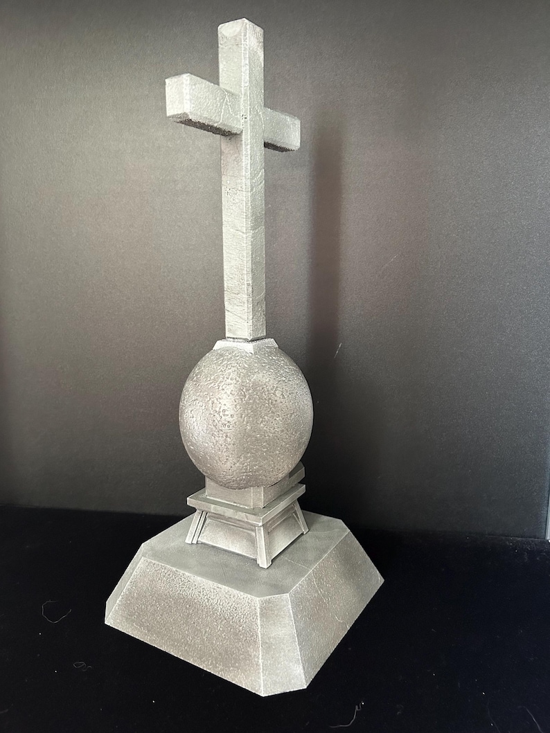 May include: A gray stone cross with a round base and a square base. The cross is on a black background.
