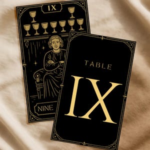 May include: Two black tarot cards with gold accents. One card features a seated figure and nine cups, labeled "IX" and "NINE." The other card reads "TABLE IX" in gold lettering. Both cards have decorative borders.