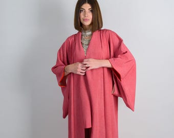 May include: A long, pink kimono with a wide, open front and long sleeves. The kimono has a subtle texture and is made of a soft, flowing fabric.