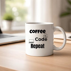 May include: White ceramic coffee mug with the words "Coffee Code Repeat" in black. The mug features a laptop icon, a coffee cup icon, and a handle. The mug is on a wooden desk next to a laptop and notepad.