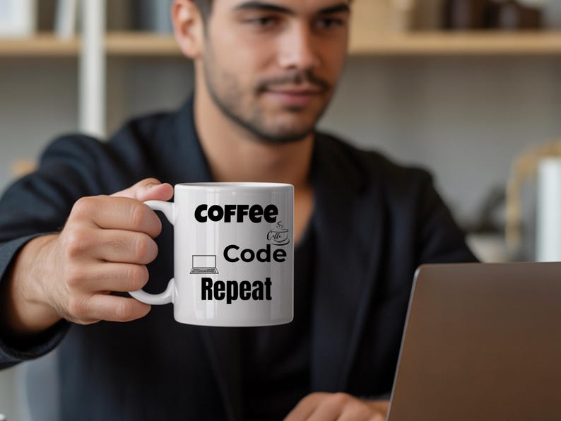 May include: White ceramic mug with the words "Coffee Code Repeat" in black, along with a laptop and coffee cup graphic. The mug is held in front of a laptop, suggesting a work or coding theme.