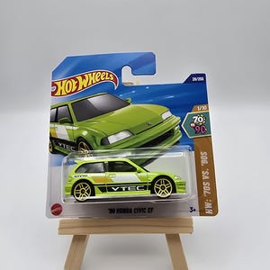 Puede incluir: Un modelo a escala Hot Wheels de un Honda Civic EF '90, en verde lima y blanco. El coche presenta ruedas doradas y la marca VTEC. El embalaje incluye el logotipo de Hot Wheels y el texto "HW: '70s vs. '90s".