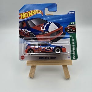Może przedstawiać: Model samochodu Hot Wheels Honda Civic Custom w przezroczystym plastikowym opakowaniu. Samochód jest niebieski, czerwony i biały z numerem 22 z boku. Opakowanie zawiera logo Hot Wheels i napis "HONDA CIVIC CUSTOM".