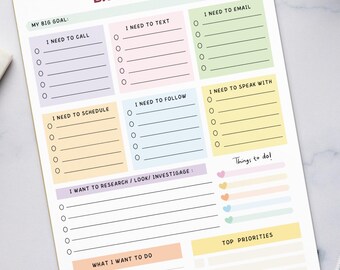 May include: A colorful Brain Dump notepad with sections for goals, calls, texts, emails, and priorities. The notepad is on a white marble surface, next to a keyboard, coffee cup, pencils, and paper clips.