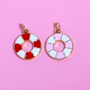 May include: Two gold-toned charms shaped like life preservers. One is red and white, the other is pink and white. Both have a circular design with a gold loop at the top for hanging. The background is a solid pink.