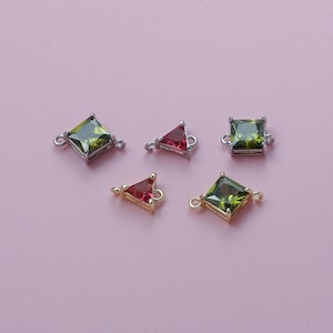 May include: An assortment of gemstone charms in various shapes: square and triangular. The gemstones are in shades of green and red, set in silver and gold-toned metal. Each charm has small loops for attaching to jewelry.