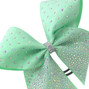 May include: A light green cheer bow with iridescent rhinestones. The bow is made of glitter fabric and has a black elastic band.