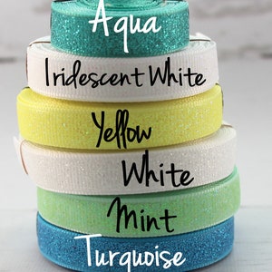May include: A stack of six different colored glitter ribbon rolls. The colors are turquoise, mint, white, yellow, iridescent white, and aqua.