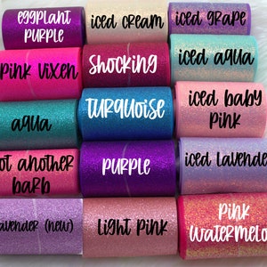 May include: A collection of 10 rolls of glitter ribbon in various colors, including pink, purple, aqua, and lavender. The ribbon is labeled with names like "Pink Vixen", "Shocking Turquoise", "Iced Grape", and "Light Pink".