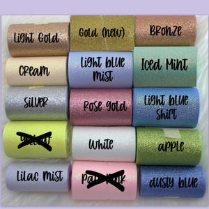 May include: A collection of 12 rolls of glitter ribbon in various colors, including light gold, gold, bronze, cream, light blue mist, iced mint, silver, rose gold, light blue shift, white, apple, lilac mist, dusty blue.