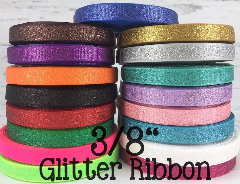 May include: A stack of 3/8 inch wide glitter ribbon in various colors, including gold, silver, purple, orange, black, red, green, pink, blue, and white. 3/8" Glitter Ribbon