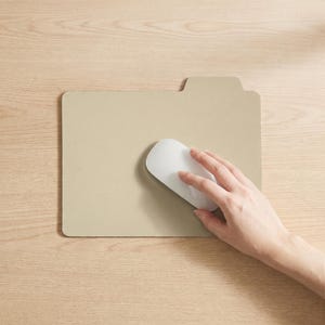 May include: A beige mouse mat shaped like a file folder with a tab on the top right corner. A smooth, white, low-profile computer mouse rests on the surface of the mouse mat, which is positioned on a light-coloured wood grain surface.