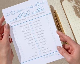 May include: A white paper game sheet with the text "would she rather" in a script font. The game sheet has a list of options for the bride-to-be to choose from. A gold pen and a notebook are in the background.