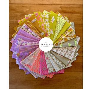 May include: A circular fan arrangement of folded fabric squares featuring diverse patterns including geometric grids, floral motifs, and small animal illustrations in shades of yellow, green, pink, purple, and grey, with a central logo reading THE THREAD MERCANTILE.