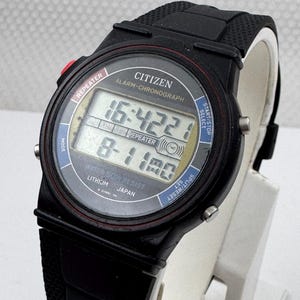 May include: A black Citizen digital watch with a textured rubber strap. The round face features a digital display showing 16:42:21 and 8-11. Text on the dial includes REPEATER, ALARM-CHRONOGRAPH, WATER 50M RESIST, LITHIUM, and JAPAN. It has side buttons.