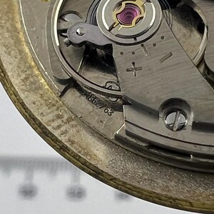 May include: Detailed view of a watch movement, revealing its complex internal workings. The image highlights metallic parts, such as gears, screws, and a balance wheel with a jewel. The serial number, 562/63, is stamped on the mechanism.