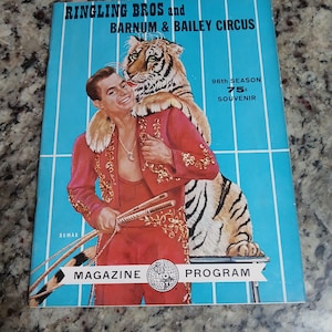 May include: Vintage Ringling Bros. and Barnum & Bailey Circus magazine program. The cover features a man in a red suit with a tiger draped over his shoulders. The magazine is blue with white stripes and text.