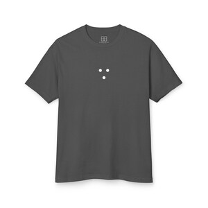 May include: A charcoal gray t-shirt with a minimalist design. The shirt features three white dots arranged in a vertical line near the center. The upper left corner of the shirt has a small white logo. The shirt has short sleeves and a crew neck.