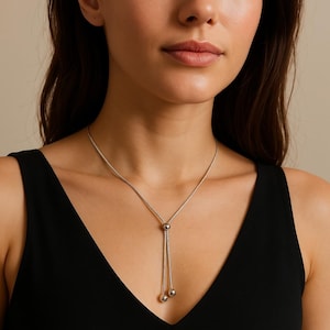 May include: A silver chain necklace with two small silver balls at the end. The necklace is worn by a person with long brown hair.