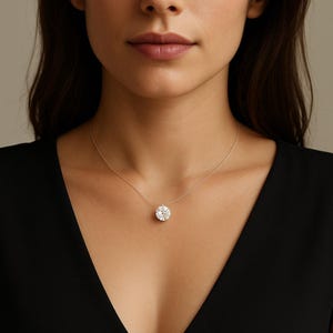 Peut inclure: Un collier en argent avec un grand pendentif rond en pierre précieuse transparente. Le pendentif est suspendu à une fine chaîne en argent. La femme porte un haut noir.