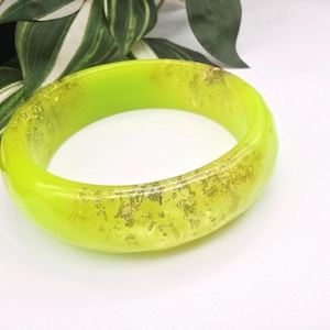 May include: A bright lime green bangle bracelet with gold leaf inclusions. The transparent resin bracelet is a striking accessory, ideal for adding a splash of colour to any ensemble. The gold leaf detail provides a touch of luxury and shimmer.