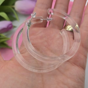 Peut inclure: Une paire de boucles d'oreilles créoles en plastique transparent. Les boucles d'oreilles sont grandes et épaisses, et elles ont une finition lisse et polie.