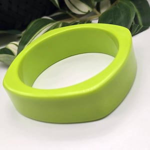 Op de afbeelding: Een limoengroene armband met een gladde, effen afwerking en een afgeronde vierkante vorm. De armband heeft een dik, robuust ontwerp met een consistente, levendige kleur over het gehele oppervlak, wat zorgt voor een strakke en eenvoudige uitstraling.