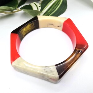 May include: A geometric bangle bracelet with a hexagonal shape. The bracelet features segments of red, cream, brown, and black. The bracelet is a bold accessory, perfect for adding a pop of color to any outfit.