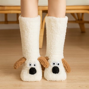 以下が含まれることがあります： クリーム色の犬の形をした、ふわふわのスリッパソックスのペア。ソックスは茶色の耳、黒い鼻、そしてギョロ目があります。ソックスは足と下腿を覆うように設計されています。