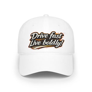 Puede incluir: Gorra de béisbol blanca con el texto "Drive fast Live boldly!" en letras negras y naranjas. La gorra tiene una visera curva y un diseño clásico de seis paneles. El texto está estilizado con una fuente temática de carreras.