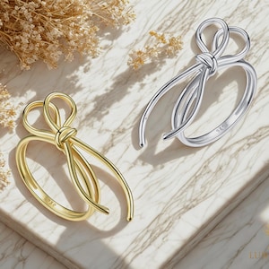 May include: Two gold and silver rings with a bow design. The rings are on a white marble surface.