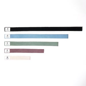 Può includere: Cinque cinturini in tessuto di diversi colori: nero, blu, verde, marrone e beige. Ogni cinturino ha una piccola etichetta bianca con la scritta "NATURAM" e un logo circolare.