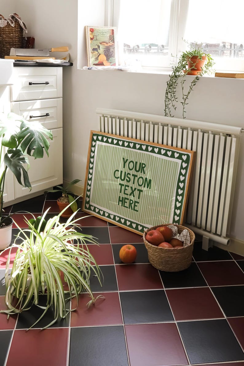 Pu&ograve; includere: Un cartello incorniciato con la scritta "YOUR CUSTOM TEXT HERE" in verde su sfondo a righe, incorniciato da un bordo di cuori verdi. Un cesto di mele e una singola mela si trovano su un pavimento piastrellato rosso e nero.