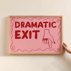 Puede incluir: Una impresión artística rosa enmarcada con las palabras "DRAMATIC EXIT" en rojo, acompañada de una mano que apunta hacia abajo. La obra de arte tiene un marco de madera clara y se muestra en una pared color crema.