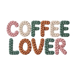 May include: The words "COFFEE LOVER" are spelled out in a knitted, textured font. The letters are in various colors, including pink, cream, green, and brown, against a white background. The letters appear to be made of thick yarn.
