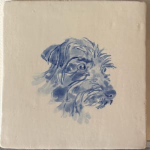 May include: Square ceramic tile featuring a blue watercolor illustration of a dog's head. The dog has a shaggy coat and a focused expression. The artwork is centered on a white background, creating a simple yet charming design.