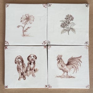 May include: Four square ceramic tiles with sepia-toned illustrations. One tile features a daisy, another a cluster of flowers, a third shows two dogs, and the last depicts a rooster. Each tile has decorative corner accents.