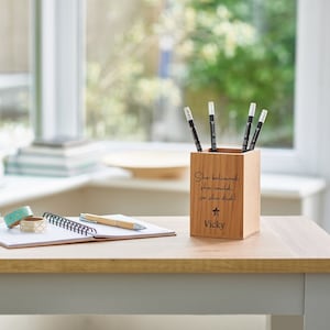 May include: A wooden pencil holder with the quote "She believed she could, so she did!" and the name "Vicky" engraved on it. The holder is filled with black pencils and is sitting on a wooden table.