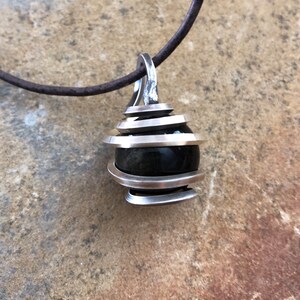 May include: A silver pendant necklace with a black gemstone encased in a spiral design.