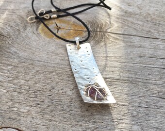 May include: A silver pendant necklace with a hammered rectangular silver plate and a purple gemstone set in a silver wire cage.